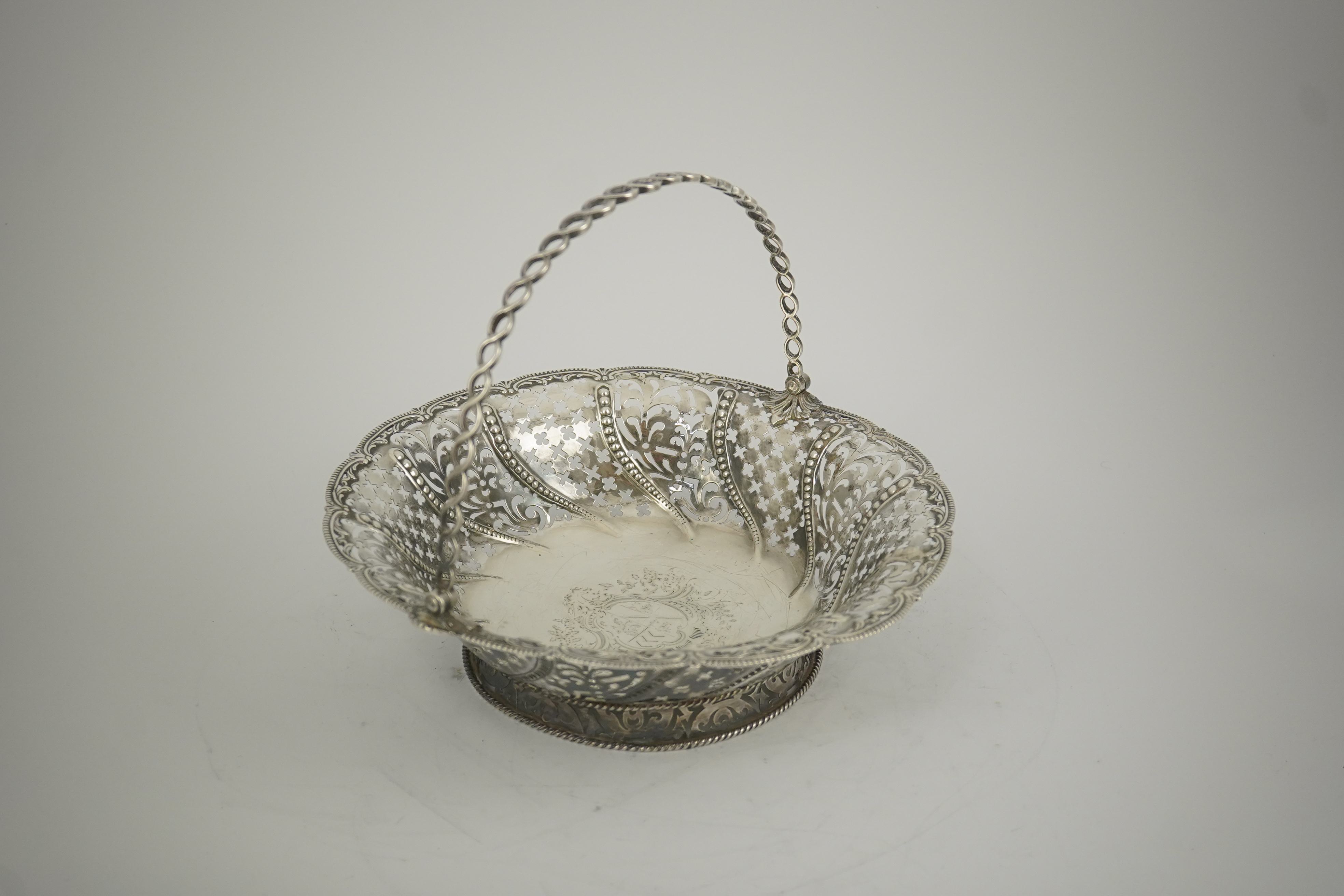 A late George II pierced silver cake basket, by William Plummer?, of shaped circular form, with engraved crest and multi ring handle, London, 1759, diameter 29.2cm, 25.5oz. (a.f.). Condition - poor